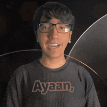 a young man wearing glasses and a t-shirt that says ayaan