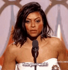 a woman in a white dress is standing in front of a microphone and says `` you gon ' wait '' .