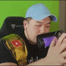 a man wearing a blue hat is sitting in a chair drinking from a bottle .
