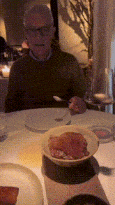 a man with glasses sits at a table with plates and bowls