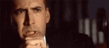 a man in a suit and tie is making a funny face while holding his hand to his mouth .