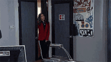 a woman in a red jacket is standing in front of a door with a sticker on it that says " de "