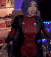 a woman with blue hair is sitting in a chair wearing a red top