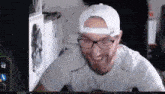 a man wearing glasses and a white hat is smiling while sitting in front of a computer screen .
