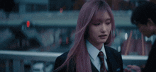 a girl with pink hair is wearing a suit and tie and talking to another girl .