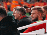 a man in a red shirt is sitting in a stadium with other men