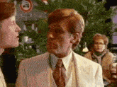 a man in a white suit and tie is talking to another man in a restaurant .