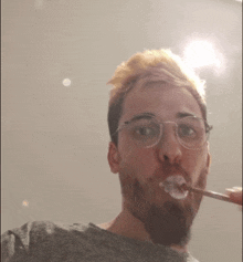 a man with glasses is brushing his teeth with toothpaste