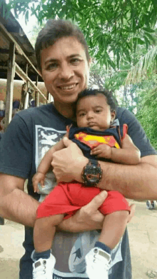 a man is holding a baby wearing a superman costume