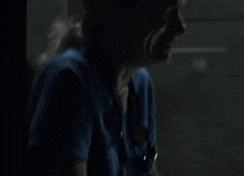 a woman in a blue shirt is crying in the dark while sitting in front of a window .