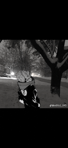 a black and white photo of a person standing next to a snow covered tree .