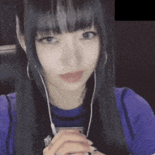 a woman wearing a purple shirt and ear buds looks at the camera