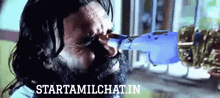a man with a beard is drinking from a blue bottle and the website starttamilchat.in is visible