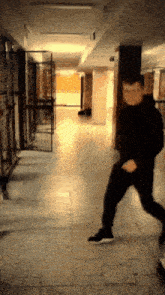 a man in a black hoodie and black pants is running in a hallway