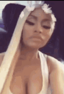 a woman with long blonde hair and a flower crown on her head is wearing a white tank top .