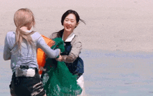 two women are playing with a green bag on the beach