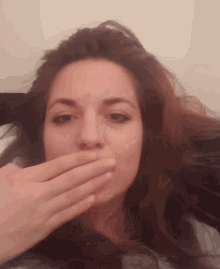 a woman covering her mouth with her hand while looking at the camera