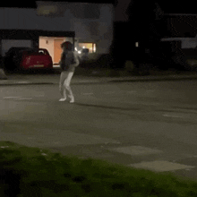 a person is walking down a street at night in front of a house .