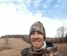 a man wearing a camo hat and scarf is smiling