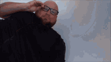 a bald man with glasses and a beard is laying on the floor .