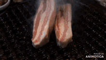 two pieces of meat are being cooked on a grill with smoke coming out of it .