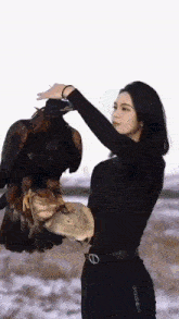 a woman in a black shirt is holding a large bird on her arm .