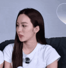 a woman is sitting on a couch wearing a white t-shirt and making a funny face .