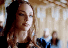 a woman with long hair and blue eyes is standing in a hallway looking at the camera .