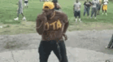 a man in a brown shirt and a yellow hat is dancing in front of a group of people .