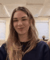 a woman wearing a cross necklace and a blue sweater smiles for the camera .