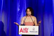 a woman stands at a podium that says new era