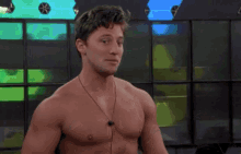 a shirtless man with ear buds around his neck looks at the camera