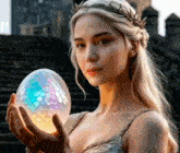 a woman with a crown on her head is holding a dragon egg in her hands