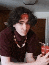 a young man wearing a headband and a necklace holds a glass of coca cola