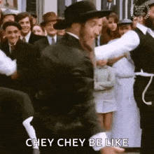 a man in a hat is dancing in front of a crowd of people and saying chey chey be like .