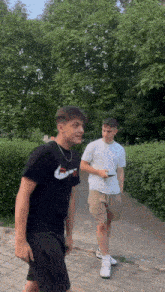 two young men are walking down a sidewalk one is wearing a black nike shirt