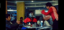 a man in a red and black shirt is sitting at a table in a restaurant with other people