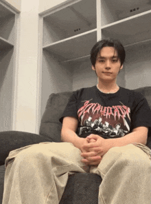 a man wearing a black t-shirt that says ' apocalypse ' on it sits on a couch
