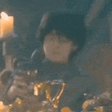 a young boy is sitting at a table with a candle in the background holding a teapot .