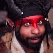 a man with a beard and red paint on his face is wearing a horned hat .