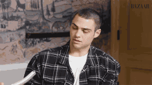 a man wearing a plaid shirt and a white t-shirt with the word bazaar on the bottom