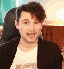a man with curly hair is sitting in a chair