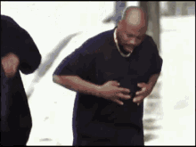 a man in a black shirt is holding his stomach while walking down the street .