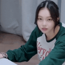 a young woman is sitting at a table wearing a green and white sweater .
