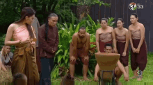 a group of people are standing around a man kneeling down in front of a large pot .