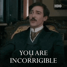a man in a suit and tie is sitting in a chair and saying you are incorrigible