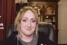 a woman is sitting in a chair with earbuds in her ears and a bookshelf in the background