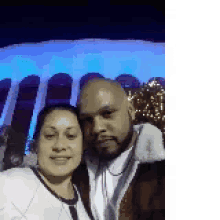 a man and a woman are posing for a selfie in front of a building with blue lights .