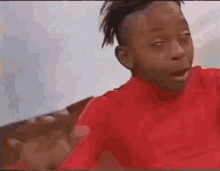 a young boy in a red shirt is making a funny face while sitting on a couch .