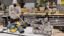 a man wearing a mask is cleaning a table with a broom and a robot with the number 16743 on it